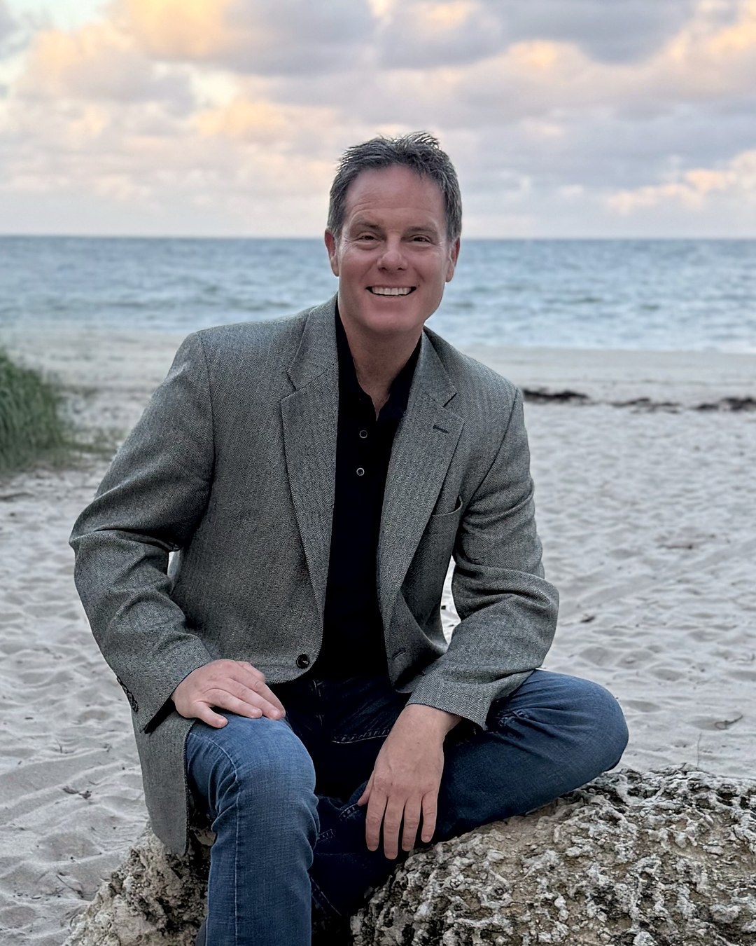 Jason Schubert, founder of Shoreline Leadership, seated on a beach at sunset